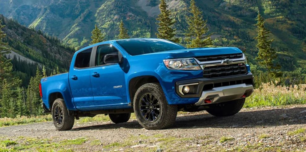 A blue 2022 Chevrolet Colorado parked on a field with foliage and mountains in the background.