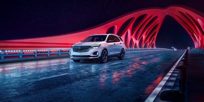A white 2024 Chevy Equinox driving at night across a red frame bridge.