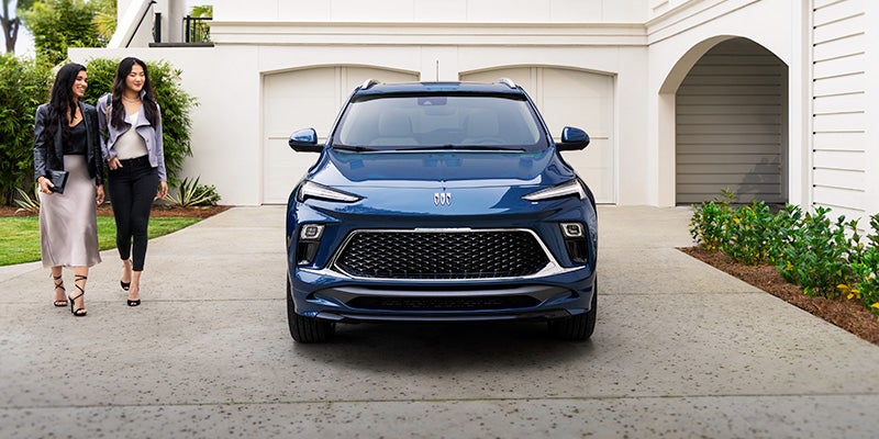 A blue 2024 Buick Encore GX parked in the driveway and the owners are walking towards it.