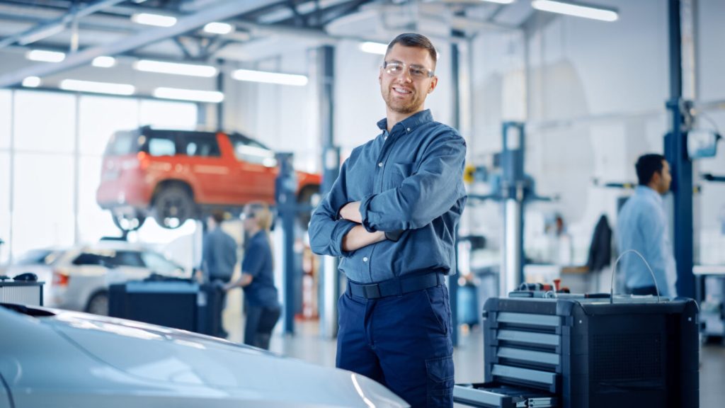 A service technician smiling in his auto repair shop.