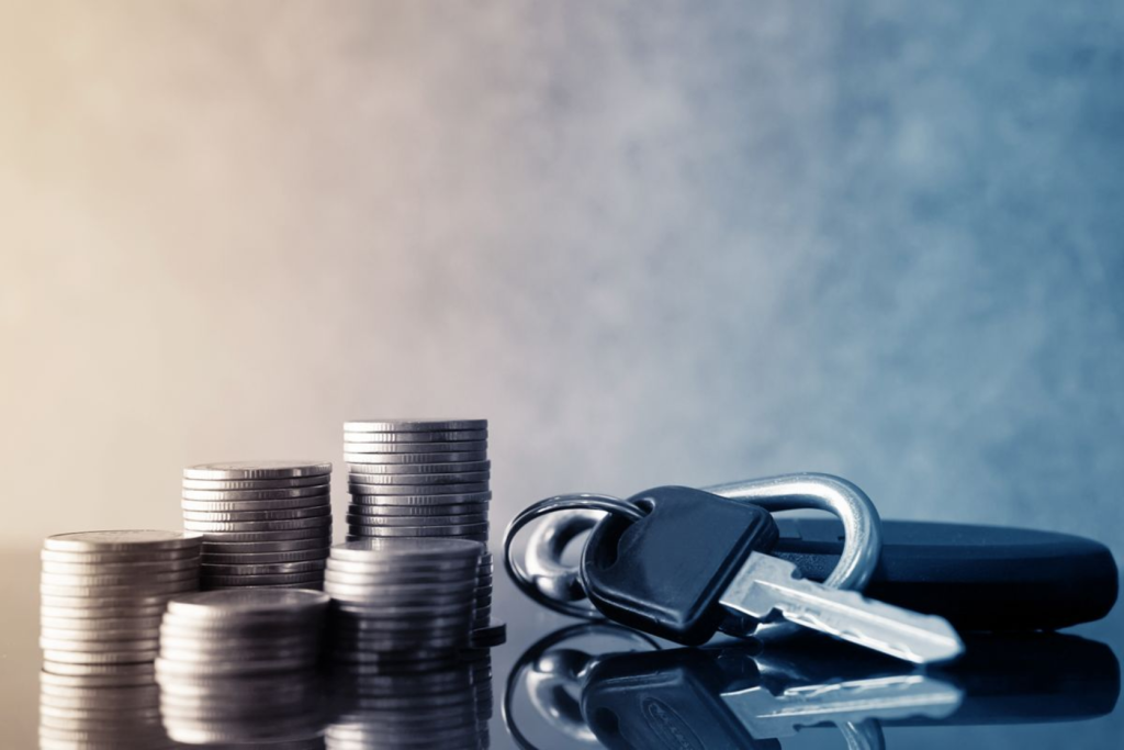 Stacks of coins next to a car key and keychain on a reflective surface.